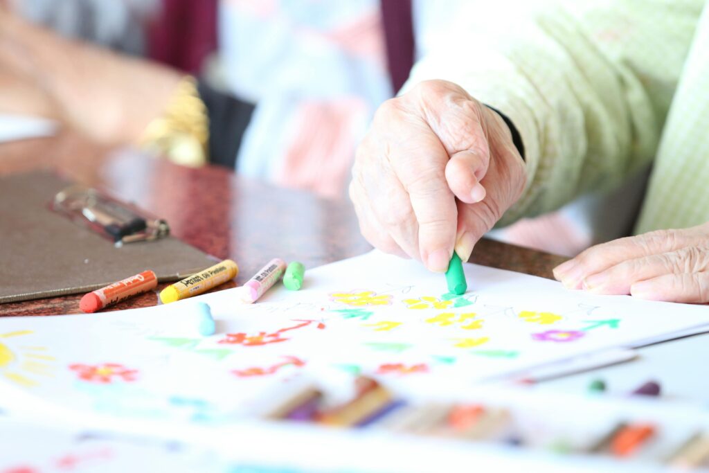 Close-up of a senior woman drawing with crayons in an art therapy session indoors.