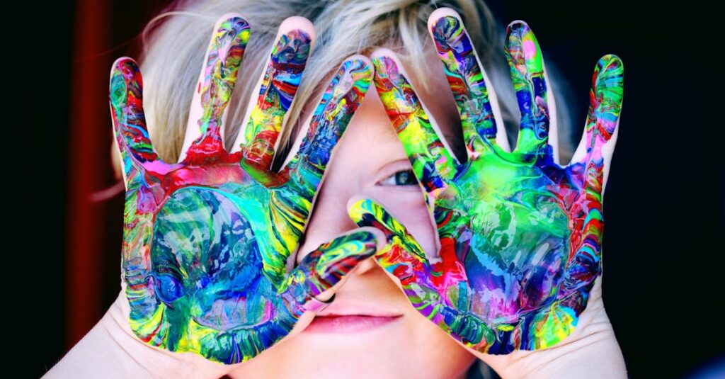 Young child holding up paint-covered hands, engaging in a sensory and kinesthetic expressive arts experience.