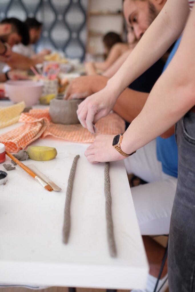 A diverse group of adults participating in a pottery workshop, focusing on hands crafting clay at a table.