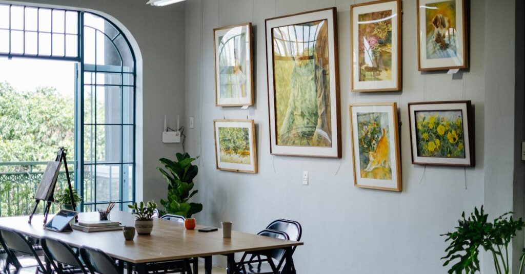 A bright home office featuring framed artwork, greenery, and a large table near a window.