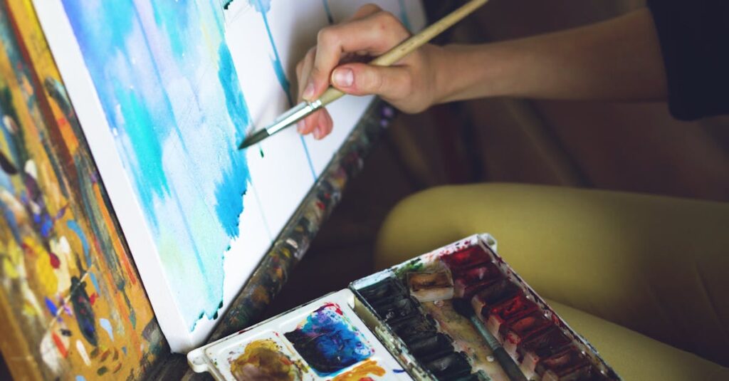 Close-up of an artist's hand painting on a canvas using watercolors with a palette.
