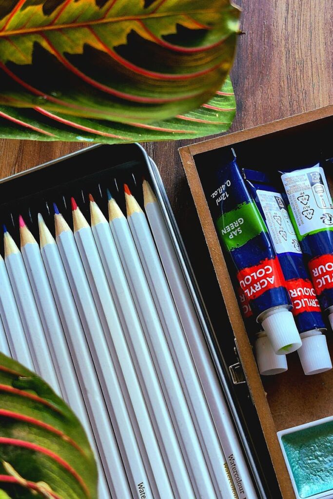 Colorful pencils and paints creatively laid out on a wooden surface with leaves.