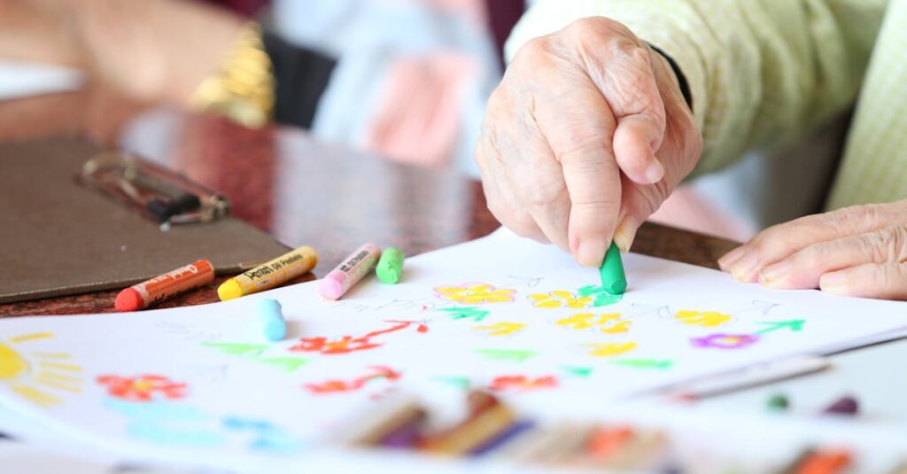Faceless elderly person with rheumatoid arthritis drawing with crayon during rehabilitation in nursing home