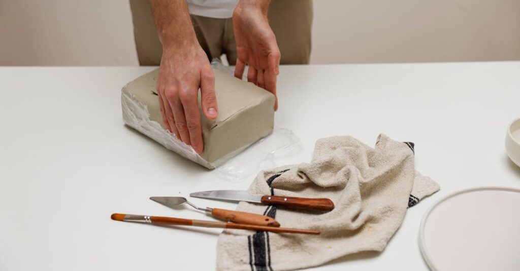 Hands preparing clay with tools on a table, ready for sculpting.